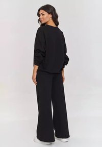 Czarna, oversize bluza z opadającymi ramionami i długimi rękawami, w połączeniu z szerokimi spodniami. Gładki materiał, luźny krój, bezszwowy tył.