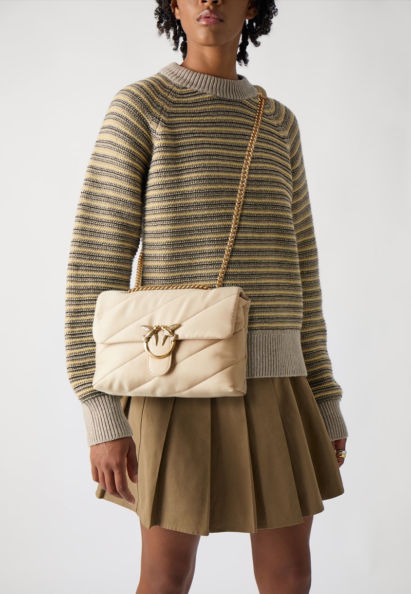 Μπεζ τσάντα με κέντημα και χρυσές λεπτομέρειες, διακοσμητικό κούμπωμα, συνδυασμένη με ζακέτα με ρίγες και πλισέ ελιωτή φούστα.