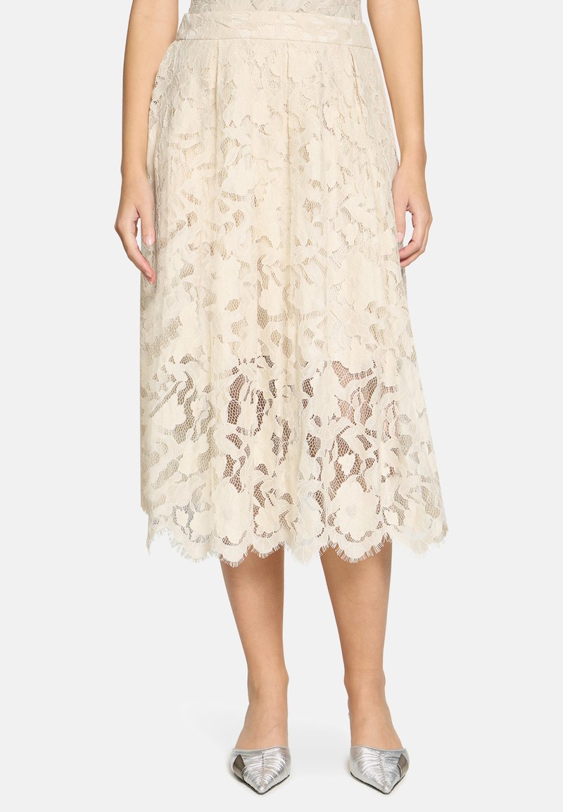 Midi-nederdel i cremefarvet blonder med blomsterprint og bølget kant. Parret med skinnende sølvfarvede spidse flade sko.