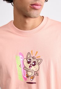 Ljust rosa T-shirt med en kartongdjur grafik med stora ögon, lekfullt uttryck och färgglad text "animals originals" i grönt och rosa.