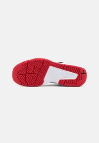 Semelle d'une basket avec un motif en caoutchouc rouge et blanc comportant le logo Nike Air et un petit logo Jumpman noir au talon.