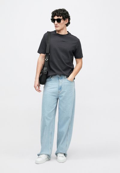 Čierne tričko s pruhmi, svetlomodré džínsové nohavice so širokými nohavicami, biele tenisky a čierna kabelka cez rameno. Modelka má tiež čierne slnečné okuliare.