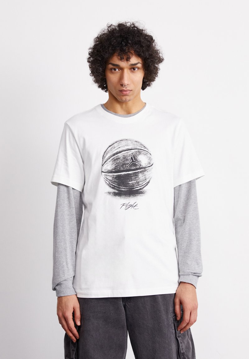 Camiseta blanca de manga corta con un gráfico de baloncesto y el texto "Flight", llevada sobre una camiseta de manga larga gris. Ajuste casual, material de algodón.