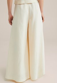 Breedbenige, crèmekleurige linnen broek met een soepele textuur, met een hoge taille en geen zichtbare sluitingen. Achteraanzicht.