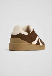 Brune ruskind sneakers med lyse beige accenter, tekstureret gummisål, rund form, og detaljer inkluderer syninger og en polstret krave.