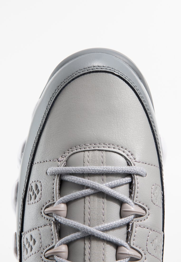 Zapatilla de cuero gris con textura suave, puntera redonda, ojales reforzados y cordones grises. Presenta sutiles acentos de logo y suela de goma en contraste.