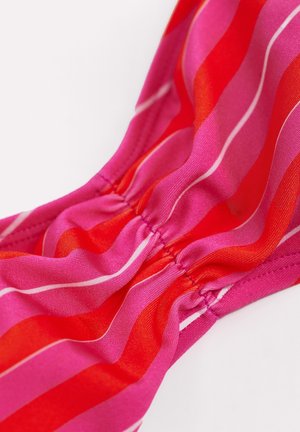 Gros plan sur un tissu rayé rose et rouge avec des lignes blanches fines, froncé au niveau d'une couture cousue créant des plis doux.