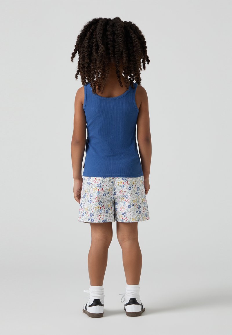 Un débardeur côtelé bleu et un short à motif floral blanc, avec des chaussettes de cheville et des baskets noir et blanc, vus de dos.