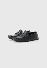Zwarte leren loafers met een gladde textuur, een ronde neus en een decoratieve metalen acccent over de wreef. Flexibele rubberen zool.