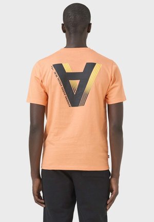 Man van achteren gezien die een perzikkleurig T-shirt met korte mouwen draagt met een grote zwartgele gestileerde "A" op de rug.