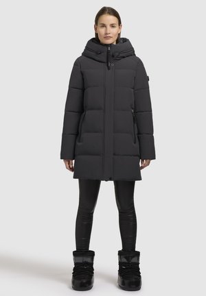 Padded black winter coat with a high collar, hood, concealed zip, and side pockets. Worn with black fitted leggings and glossy black boots.