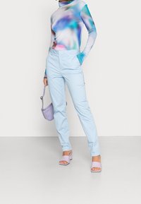 Vaaleansiniset räätälöidyt housut yhdistettynä moniväriseen liukuvärisävyiseen pitkähihamaiseen paitaan. Asusteina vaaleanvioletti laukku ja siihen sopivat korkokengät.