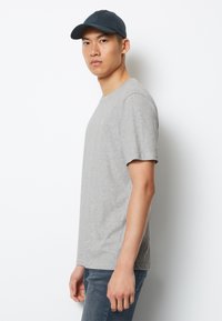 Tricou din bumbac gri deschis, cu mâneci scurte și guler rotund, purtat cu blugi albaștri și o șapcă de baseball bleu închis.