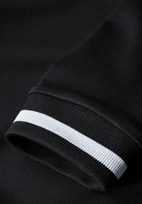 Svart atletisk ärm med ribbad textur, försedd med en vit randaccent längs ärmslutet. Tyget verkar mjukt och slätt.