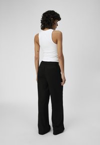 Pantalons larges noirs avec une taille élastique, associés à un haut sans manches blanc ajusté, mettant en valeur une texture de tissu lisse.