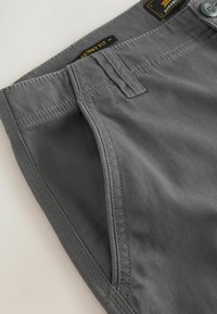 Graue Skinny-Fit-Hosen mit detaillierten Nähten, Gürtelschlaufen, Fronttasche und Knopfverschluss auf einem hellen Hintergrund.