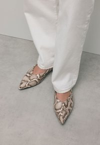 Puntige flats met een slangenprint in beige en bruintinten, gemaakt van synthetisch materiaal, gecombineerd met witte opgerolde jeans.