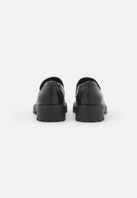 Sapatos de couro pretos com um salto baixo, bico redondo e um acabamento suave. Apresenta detalhes texturizados contrastantes no salto e nos lados.