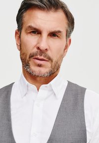 Szary kamizelka na białej koszuli, z kołnierzykiem rozpostartym i zapinaniem na guziki. Gładki materiał o subtelnej fakturze i prostych liniach.