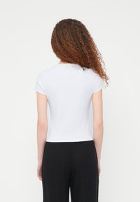 Άσπρο εφαρμοστό τοπ με κοντά μανίκια και στρογγυλή λαιμόκοψη με ραβδωτή υφή, συνδυασμένο με μαύρο φαρδύ παντελόνι, από πίσω όψη.