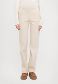 Pantalons beige ajustés à coupe droite avec passants de ceinture. Tissu doux, poches latérales et un design épuré et simple. Associés à des chaussures à plateforme marron.