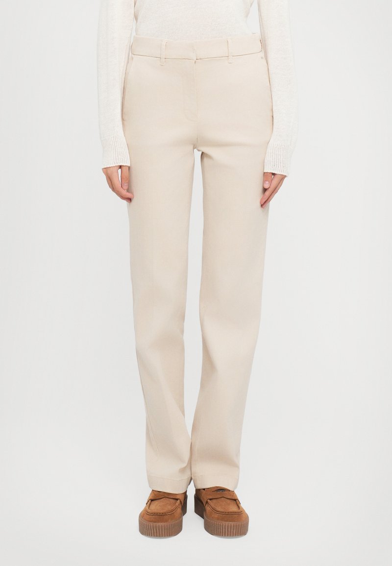 Pantalons beige ajustés à coupe droite avec passants de ceinture. Tissu doux, poches latérales et un design épuré et simple. Associés à des chaussures à plateforme marron.