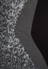 Grått tyg med silverpaljetter på ena sidan, som övergår till solid mörkgrå och svarta sektioner, som visar upp olika texturer och mönster.