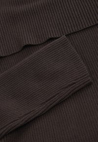 Brauner, gerippter Stoff mit einer Textur aus vertikalen Linien. Oben mit einem wellenförmigen Randdetail und einem glatten, flachen Abschnitt.