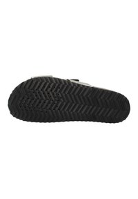 Semelle de chaussure en caoutchouc noir avec un motif en chevrons, présentant des nervures et de petites perforations pour améliorer l'adhérence et la flexibilité.