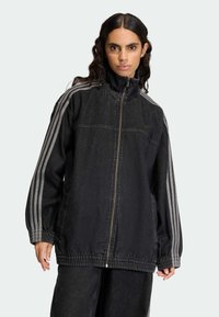 Črno denim jakna z visokim ovratnikom, z zadrgo po celotni dolžini in elastičnimi manšetami. Ima sive črte ob rokavih ter sproščen, ohlapen kroj.
