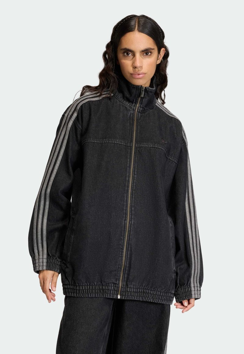 Črno denim jakna z visokim ovratnikom, z zadrgo po celotni dolžini in elastičnimi manšetami. Ima sive črte ob rokavih ter sproščen, ohlapen kroj.