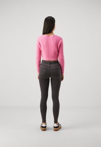 Pull rose court avec une finition texturée, associé à un jean slim gris foncé. Le modèle porte des baskets noires et blanches.