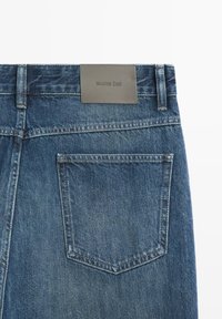 Retro dei jeans di denim blu con una tasca a toppa singola e un'etichetta in pelle grigia cucita sulla cintura.