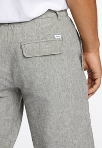 Pantalons en lin gris clair avec une poche arrière à rabat. Le tissu a une finition texturée, mettant en avant un design décontracté.