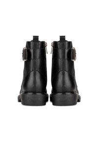 Un paio di stivali alla caviglia in pelle nera con fibbie e cerniere visti da dietro su uno sfondo bianco.