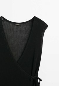 Zwarte mouwloze gebreide wikkeltop met een diepe V-hals en een zijsluiting met strik, op een witte achtergrond.