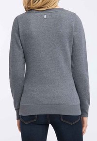 Sudadera gris fabricada en tejido suave, con cuello redondo, mangas largas y dobladillo acanalado. Una pequeña etiqueta con el logo es visible en la parte de atrás.