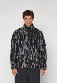 Veste en polaire noire et grise avec un motif texturé, fermeture éclair intégrale, col haut et coupe décontractée. Elle présente des manches longues et des poches.