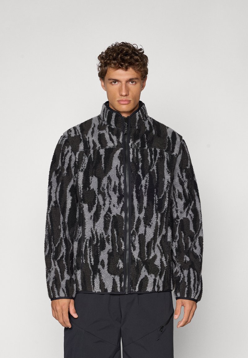 Veste en polaire noire et grise avec un motif texturé, fermeture éclair intégrale, col haut et coupe décontractée. Elle présente des manches longues et des poches.