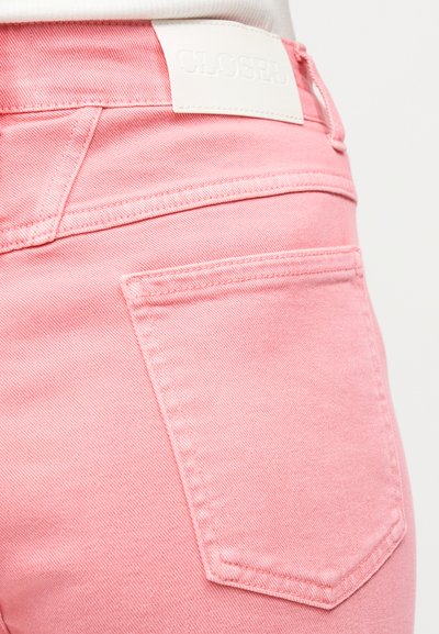 Κοντινό πλάνο πίσω τσέπης από ροζ τζιν και λευκή ετικέτα μάρκας στη μέση σε λευκή κορυφή.