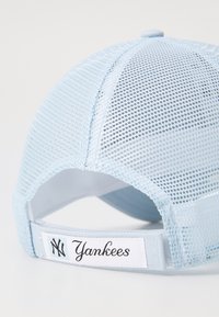 Boné de basebol azul claro com tecido em malha, visera curva e strap ajustável, apresentando um rótulo branco com "Yankees" em script preto.