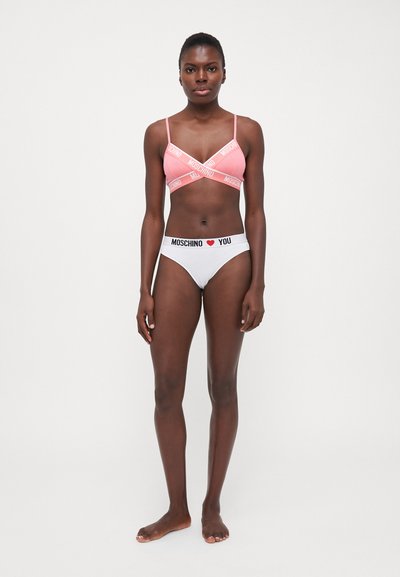 Bralet roz cu benzi albe cu logo și chiloți albi asortați cu o bandă neagră cu logo, ambele prezentând un material neted și elastic.