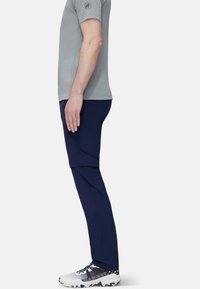 Sidosyn på en person som bär en grå kortärmad skjorta, marinblå avtagbara byxor och vita vandringsskor med svarta accenter.