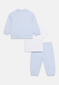 Ανοιχτό μπλε φούτερ, αντίστοιχο παντελόνι φόρμας και λευκό κοντομάνικο μπλουζάκι, όλα απλωμένα επίπεδα σε λευκό φόντο.