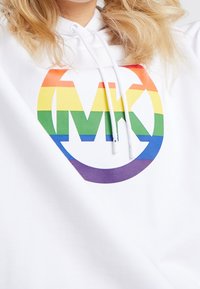Sweat à capuche blanc arborant un grand logo "MK" en dégradé arc-en-ciel. Conçu avec une texture douce et une capuche à cordon de serrage.