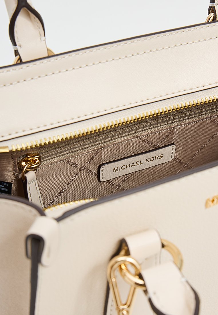 Beige Lederhandtasche mit einem Innenfach, das eine Reißverschlusstasche, goldfarbene Hardware und ein sichtbares Markenlabel umfasst. Texturierte Futter mit wiederkehrendem Logo-Muster.