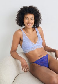 Bralette en dentelle lavande avec un décolleté en V profond et un string en dentelle bleue assorti, présentant des motifs complexes et des textures douces.