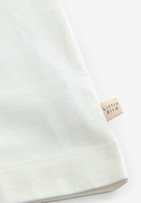 T-shirt di cotone color crema chiaro con maniche corte, caratterizzato da un orlo cucito e una piccola etichetta tessuta con "Little Bird" sul lato.