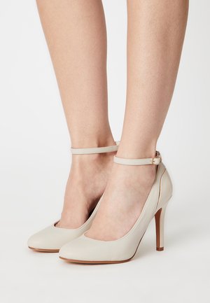 Escarpins beiges en cuir lisse, à bout rond et avec des brides de cheville ornées d'une boucle en ton doré.