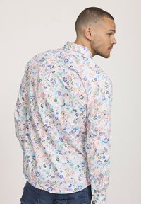 Chemise à boutons en tissu léger avec un imprimé floral coloré dans les tons de rose, bleu et vert. Dos en vert épinard avec un col classique et des manches longues.